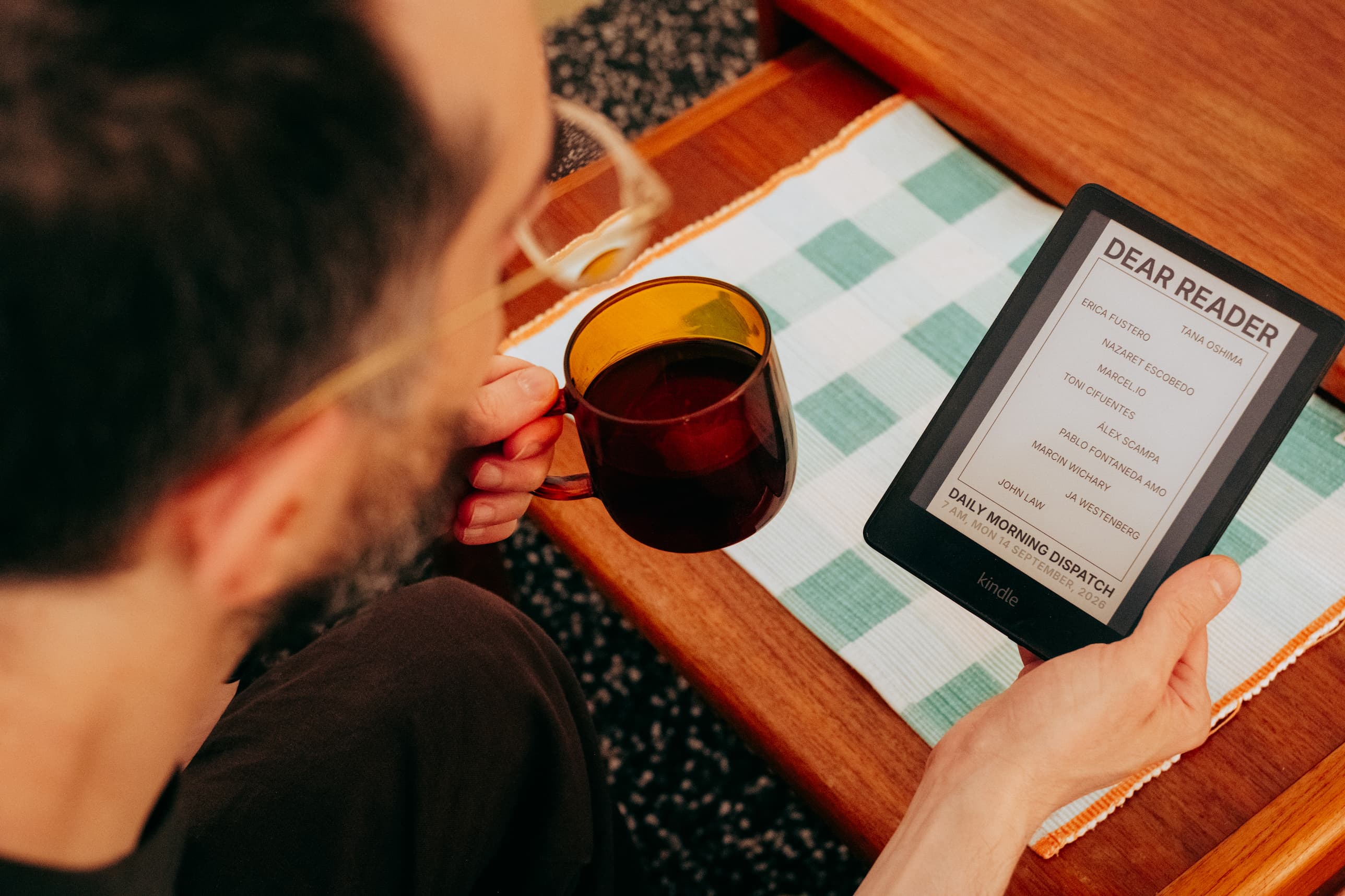 Photograph showing Javier sitting with a cup of coffee in one hand and his daily e-ink book with blogs in the other
